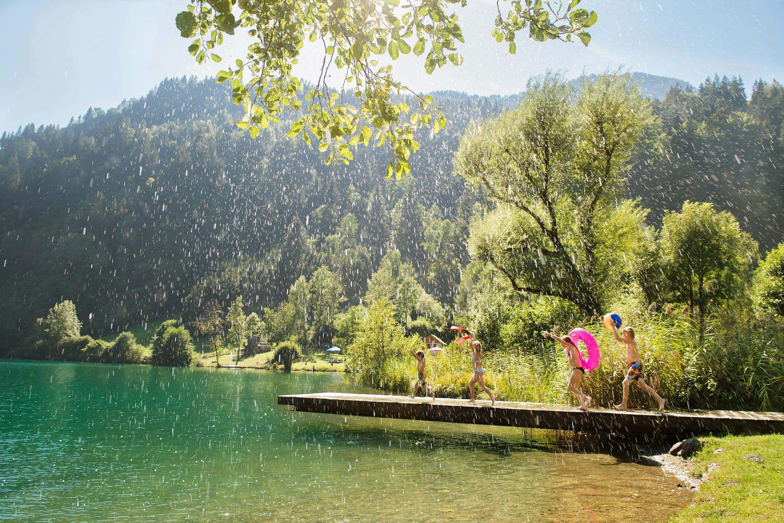 Kinder spielen und springen ins Wasser an einem sonnigen See in Kärnten