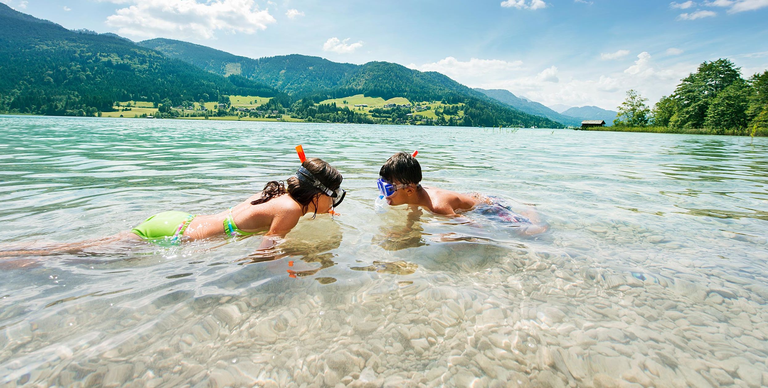 Zwei Kinder schnorcheln im klaren Wasser eines Kärntner Badesees