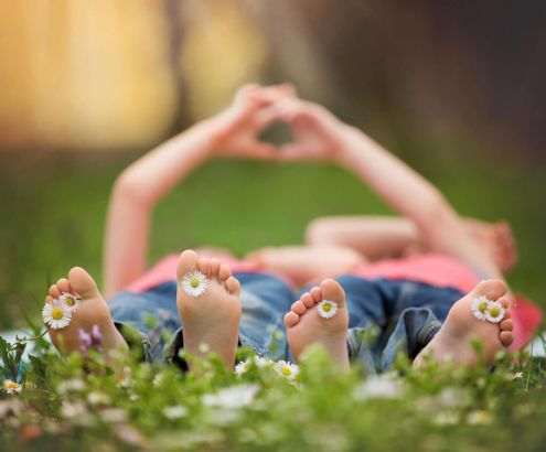 Kinder halten Herz aus ihren Finger mit Gänseblümchen zwischen den Zehen