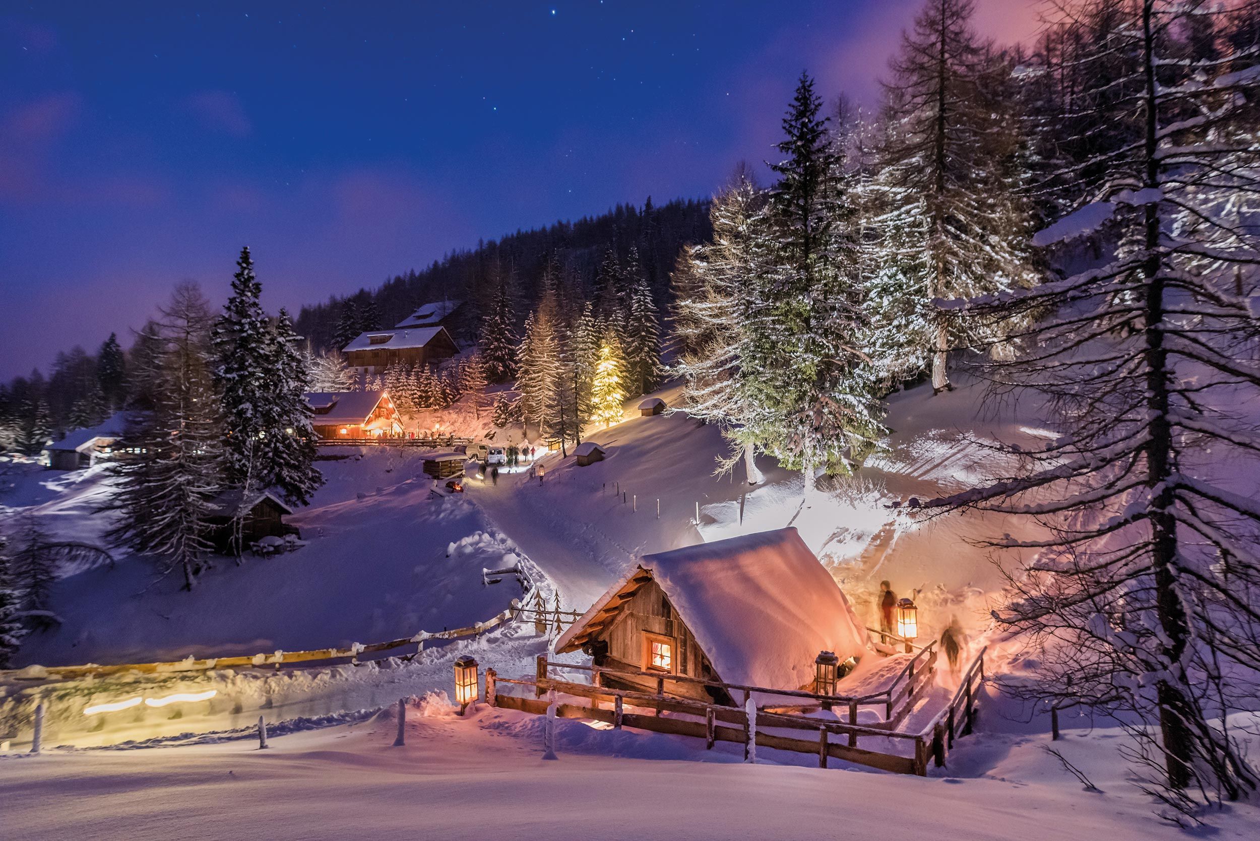 Winterlandschaft am Katschberger Adventweg mit festlich beleuchteten Hütten und verschneiten Bäumen